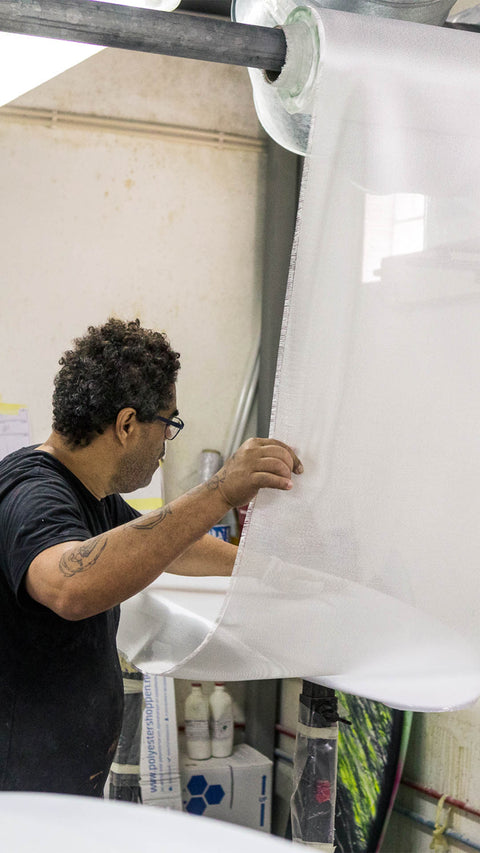 A man laying fiberglass cloth on a surfboard. 