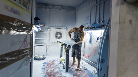 A man sanding a surfboard in a factory. 